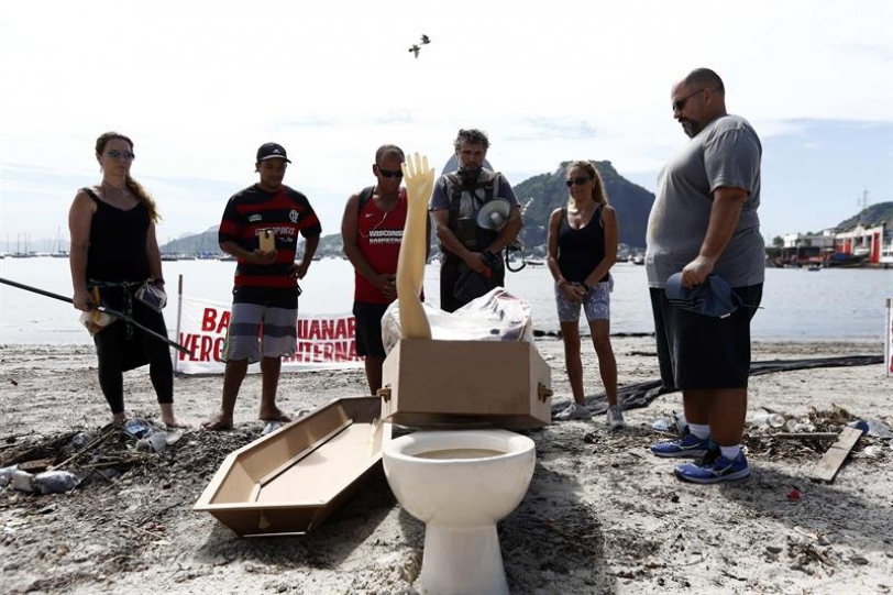 El biólogo Mario Moscatelli (c) junto a manifestantes observan un retrete, basura y un falso brazo encontrados esta semana en el lugar, durante un acto simbólico en la ensenada de Botafogo para enterrar la Bahía Guanabara, sede de vela en los Olímpicos, debido a la contaminación hoy, sábado 27 de febrero de 2016, en la playa de Botafogo en Río de Janeiro. EFE/Marcelo Sayão